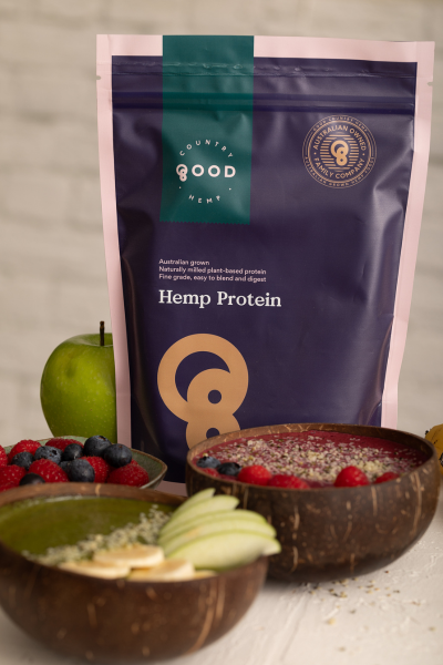 Packet of Australian hemp protein powder beside a fresh apple and a green smoothie bowl made with spinach, hemp, and yoghurt, topped with sliced banana and sprinkled with hemp seeds
